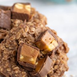 A no-bake oatmeal cookie topped with chopped pieces of chocolate and caramel candy, shown in close-up on a light background.