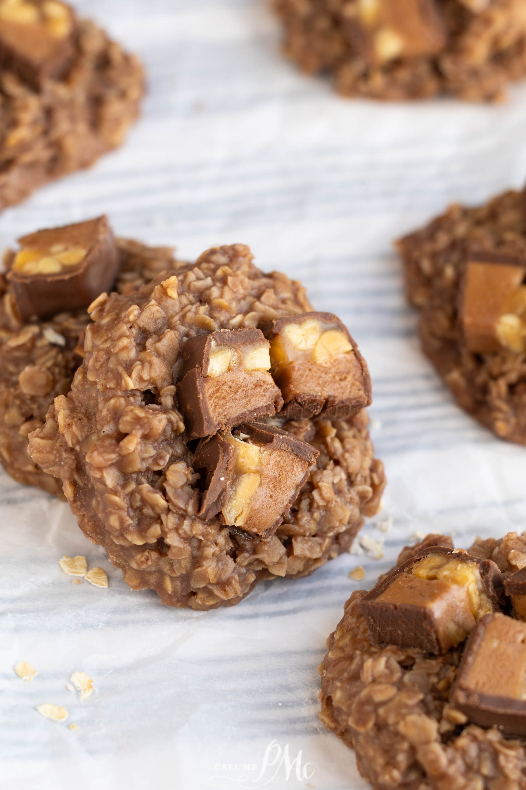 Close-up of a dessert topped with pieces of chocolate and peanut candy, arranged on a white parchment surface.