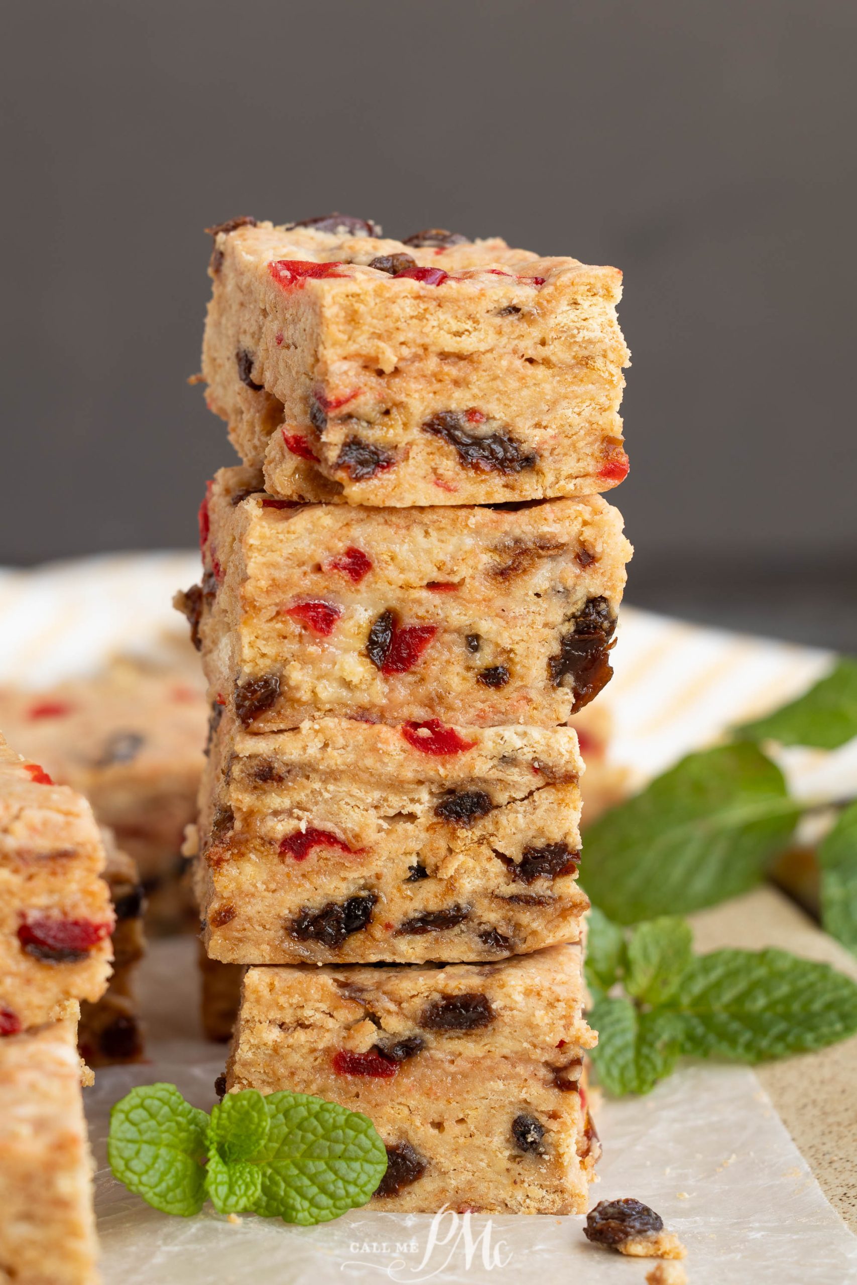 A stack of Christmas Icebox Fruitcake bars with visible pieces of dried fruit sits on a plate, garnished with fresh mint leaves.