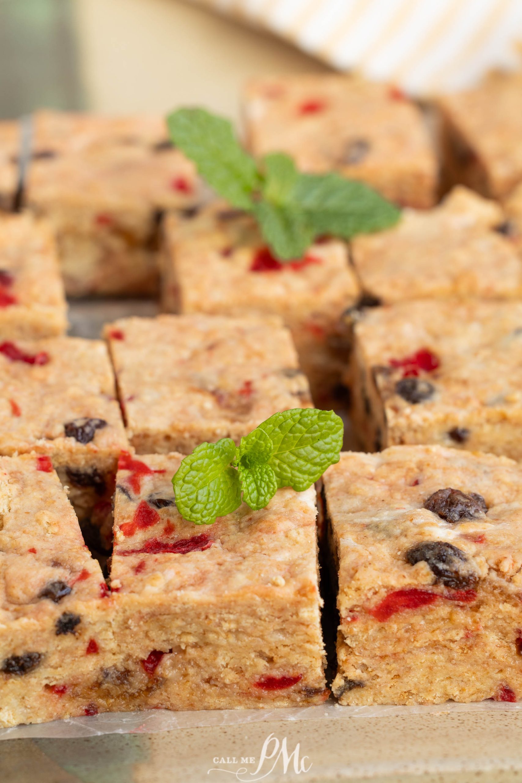 Close-up of sliced Christmas Icebox Fruitcake bars with visible fruit pieces, garnished with a fresh mint sprig on top of one piece.