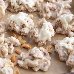 Clusters of Clodhopper Candy—white chocolate-coated snack mix—are arranged on a parchment-lined baking sheet.