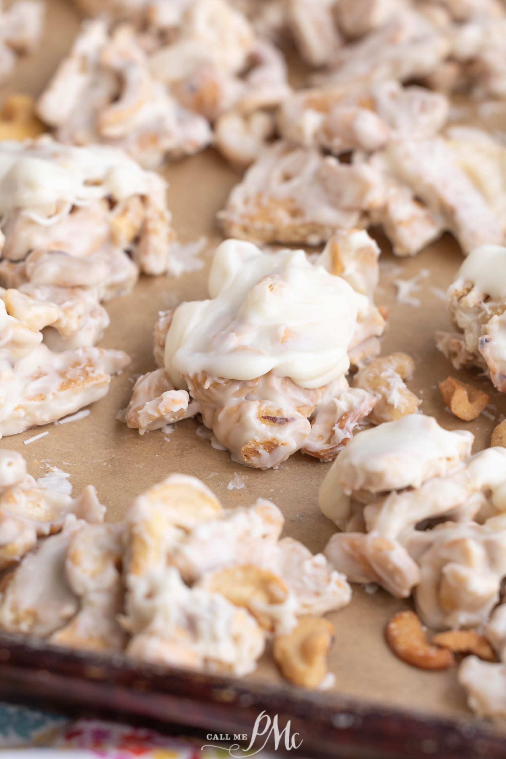 Clusters of white chocolate-covered cereal and cashews, just like classic Clodhopper Candy, are spread on a parchment-lined baking sheet.