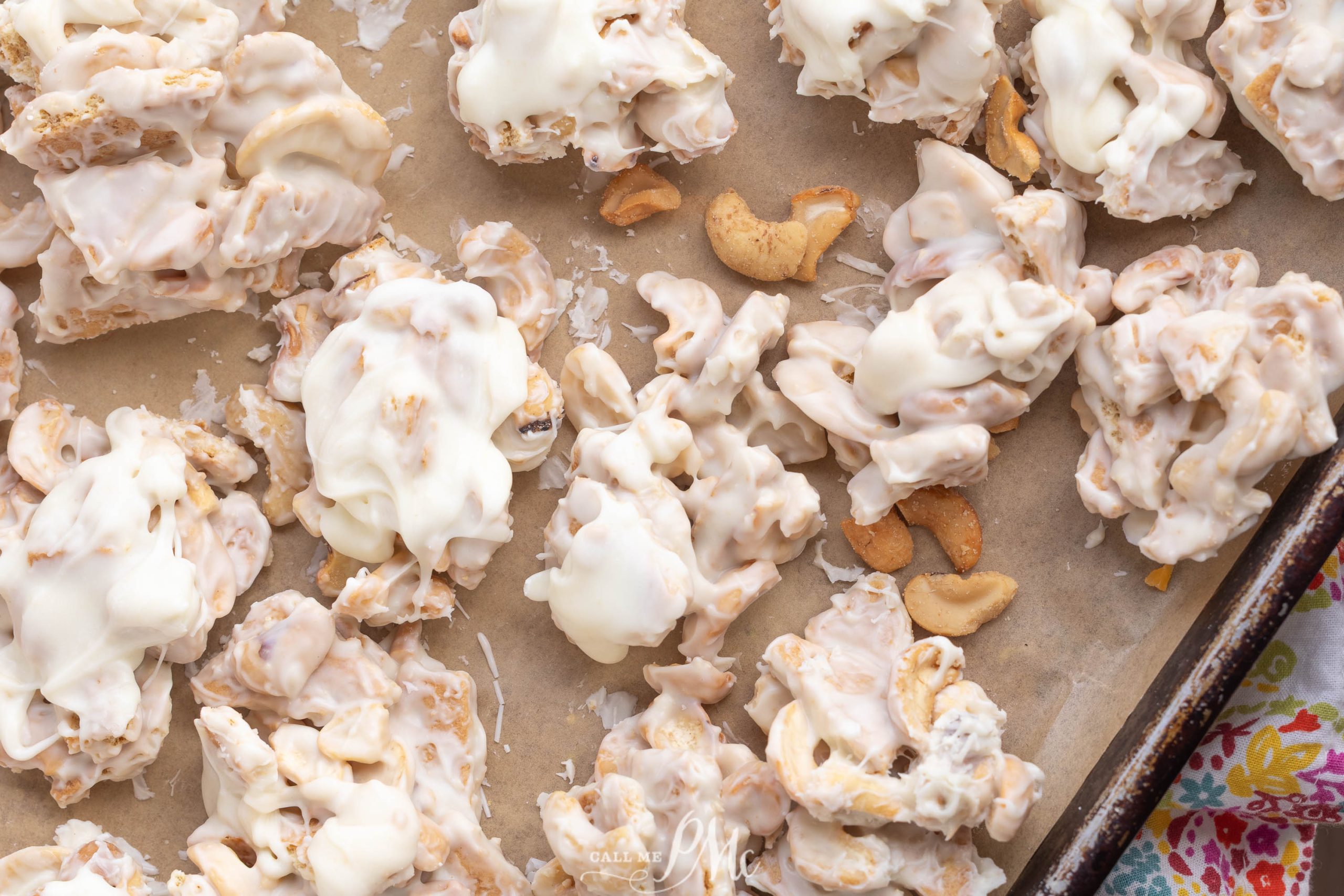 Clodhopper Candy clusters of cereal and cashews are coated in white chocolate and spread out on a sheet of parchment paper.