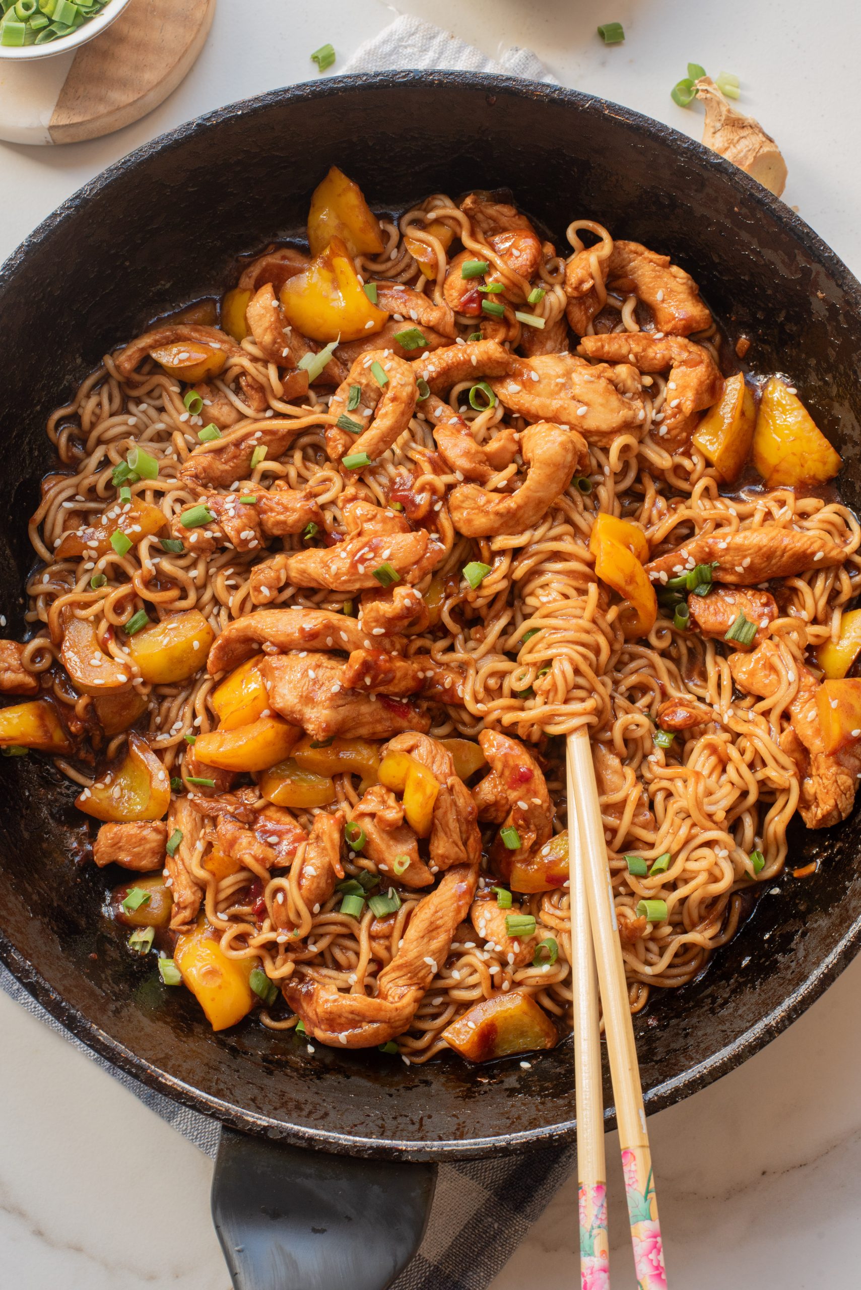 A skillet filled with Chicken Dragon Noodles—stir-fried noodles, sliced chicken, yellow bell peppers, and green onions—with chopsticks resting on the side.