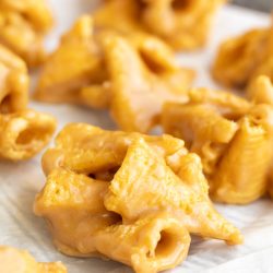 Clusters of butterscotch-coated cornflake cookies and crunchy peanut bugles are arranged on a sheet of parchment paper.