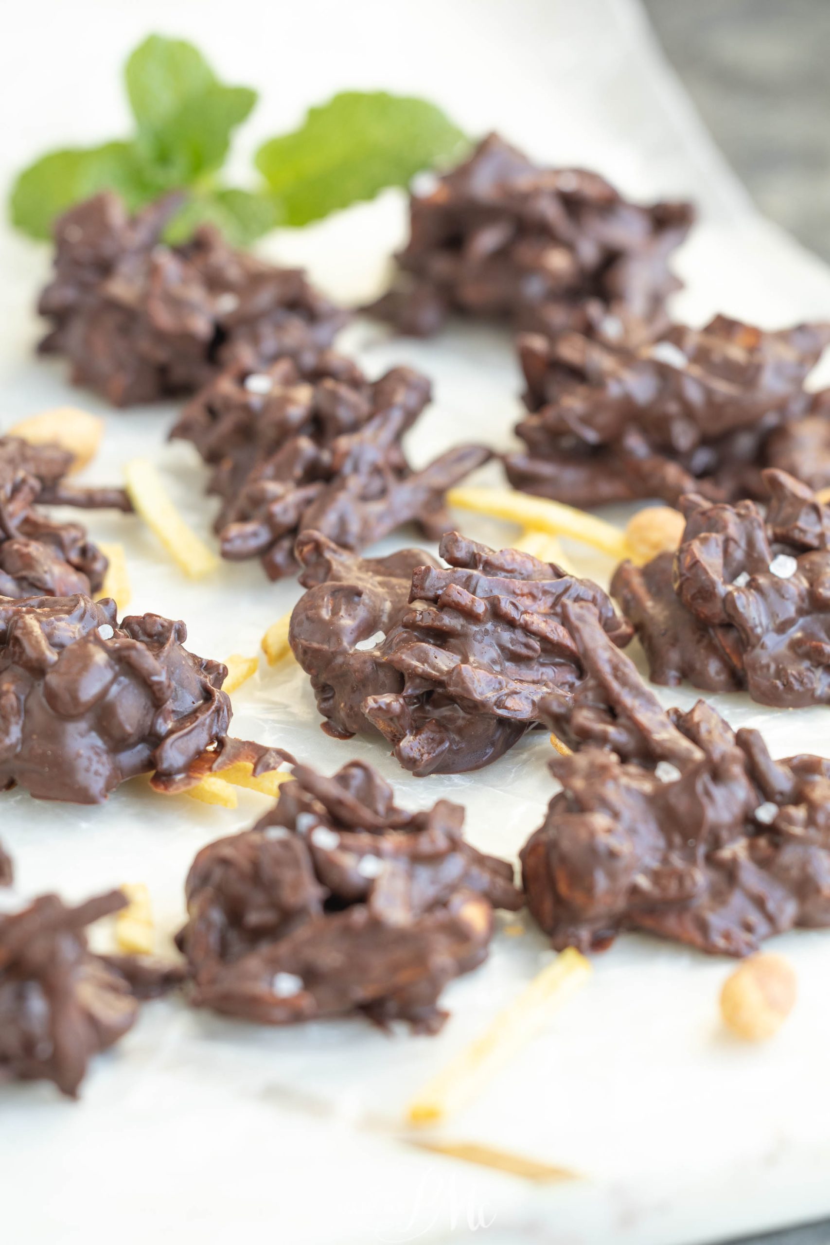 Clusters of Shoestring Potato Chip Haystacks are arranged on parchment paper, with a sprig of mint in the background.
