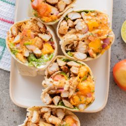 Five sliced Mango Salsa Jerk Chicken Wraps filled with grilled chicken, lettuce, diced tomatoes, red onions, and shredded cheese are arranged on a rectangular white plate.
