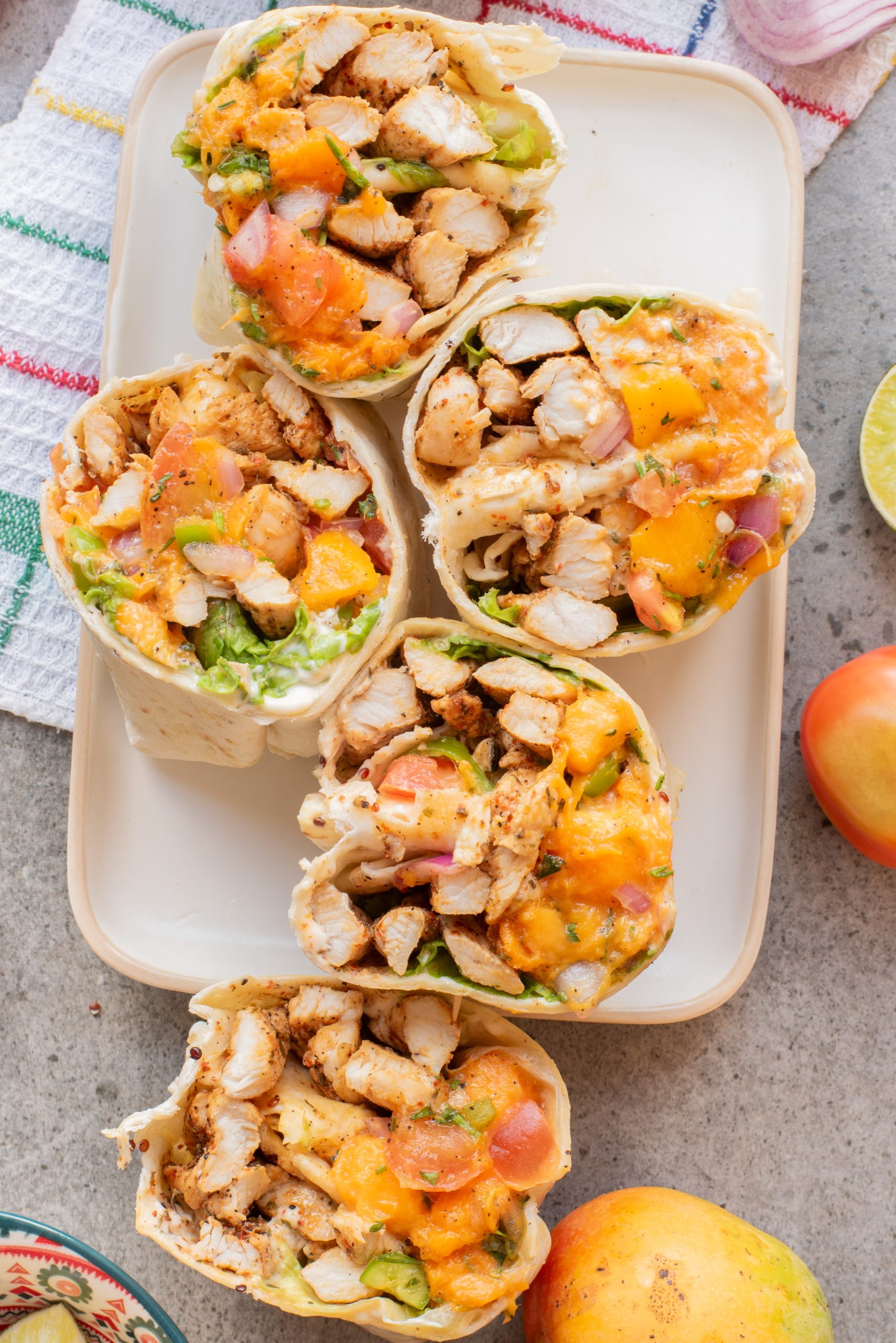 Five sliced lunch filled with grilled chicken, lettuce, diced tomatoes, red onions, and shredded cheese are arranged on a rectangular white plate.