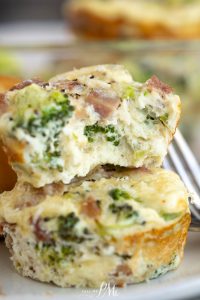 Two Muffin Tin Egg Bites with broccoli and ham are stacked, the top one partially bitten to reveal the fluffy interior.