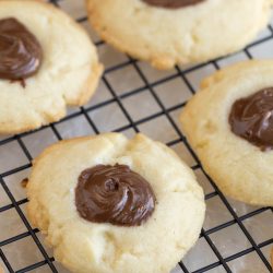 Nutella shortbread thumbprint cookies with a chocolate center are cooling on a black wire rack.