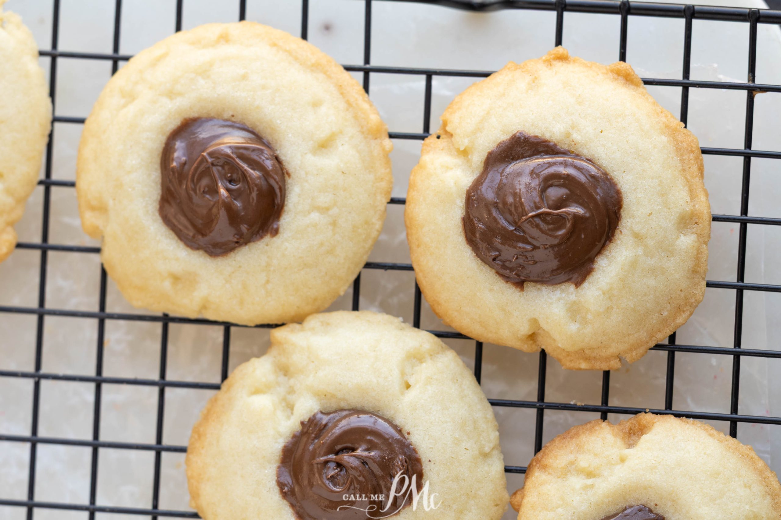 Three Nutella shortbread thumbprint cookies with chocolate centers rest on a black wire cooling rack.