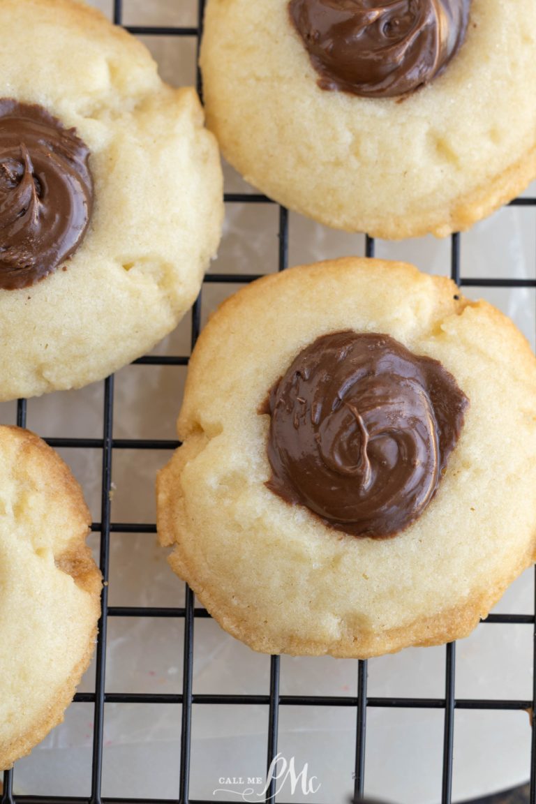 Three Nutella shortbread thumbprint cookies with a dollop of melted chocolate in the center are cooling on a black wire rack.
