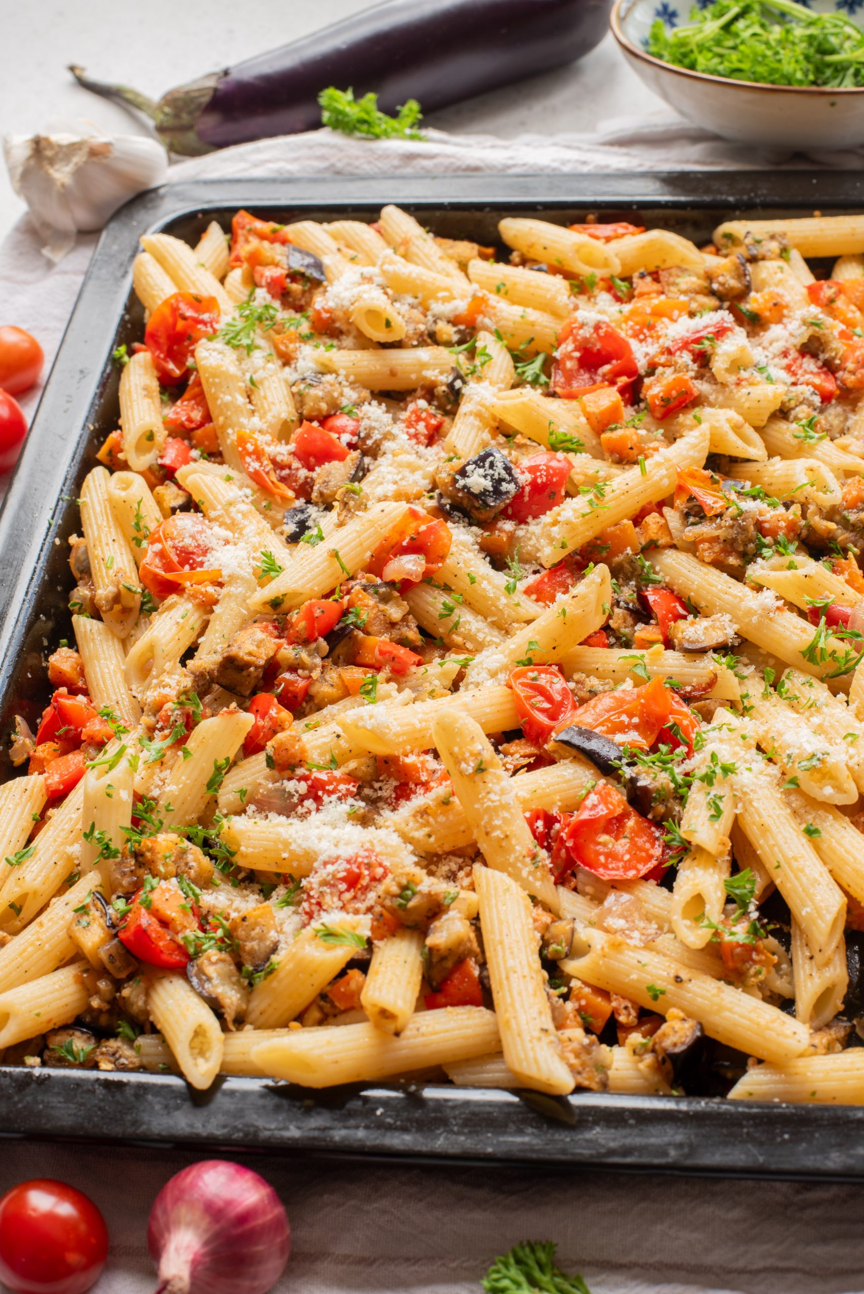 Baking tray filled with Sheet Pan Mediterranean Vegetable Pasta with fresh ingredients visible around the tray.