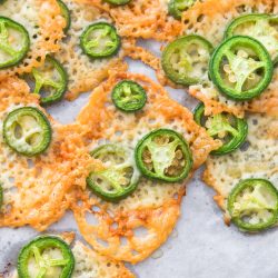 Keto Jalapeno Cheese Crisps baked to perfection and topped with sliced jalapeños, served on parchment paper.