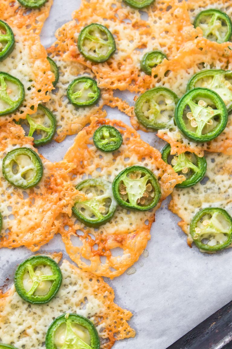 Keto Jalapeno Cheese Crisps baked to perfection and topped with sliced jalapeños, served on parchment paper.