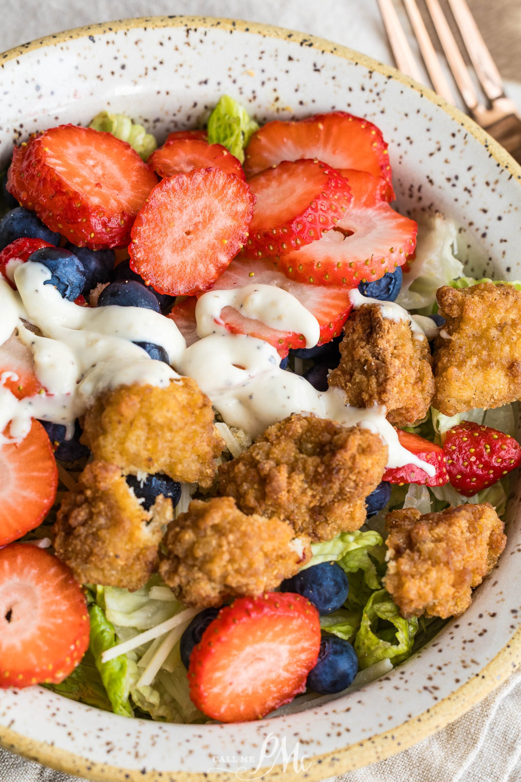 A bowl of Chicken Berry Poppy Seed Salad with fried chicken pieces, fresh strawberries, blueberries, crisp lettuce, and a drizzle of creamy dressing.