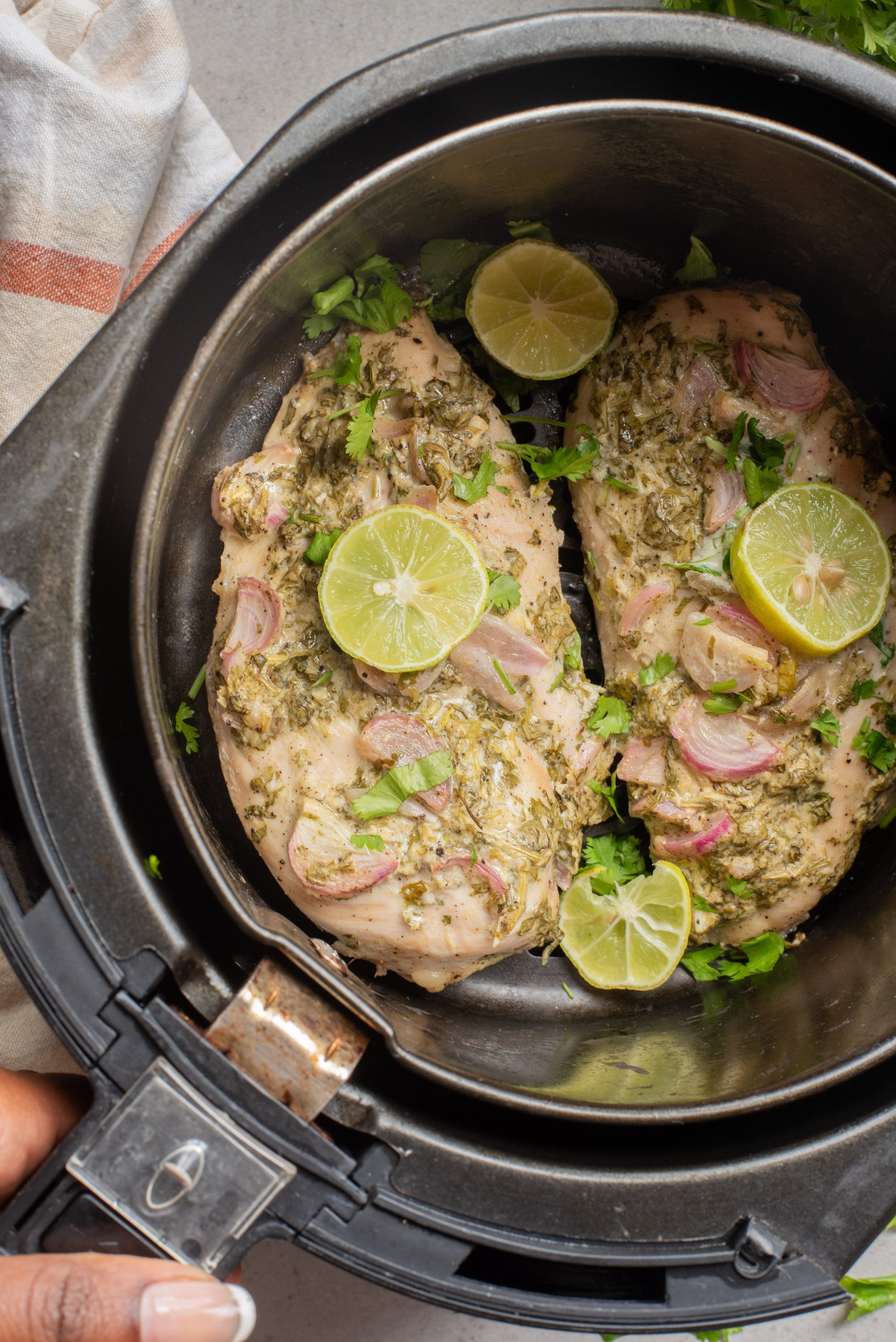 Protein garnished with herbs, sliced shallots, and lime rounds inside an air fryer basket.