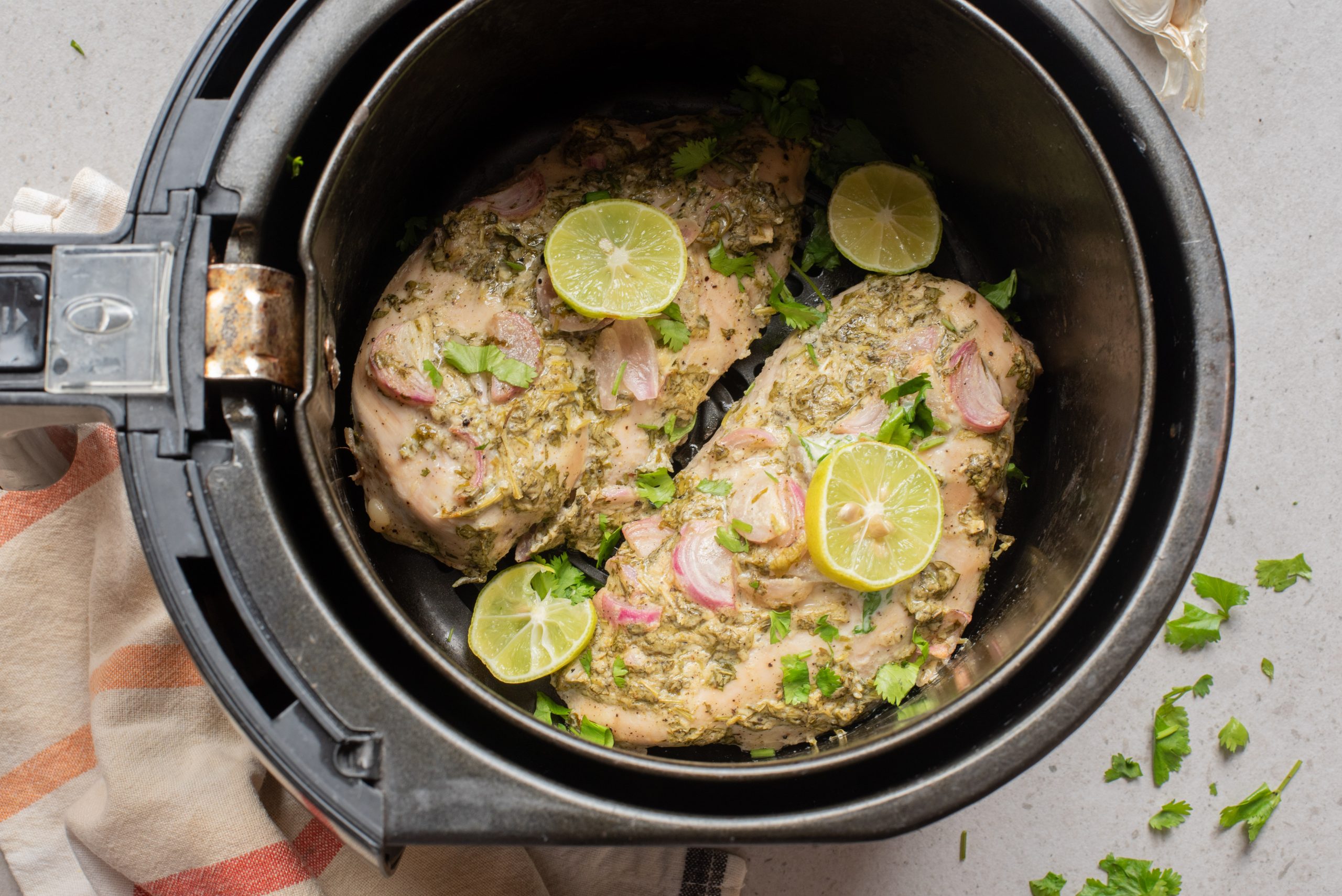 Two seasoned Marinated Yogurt Herb Chicken breasts topped with lime slices and herbs inside an air fryer basket.