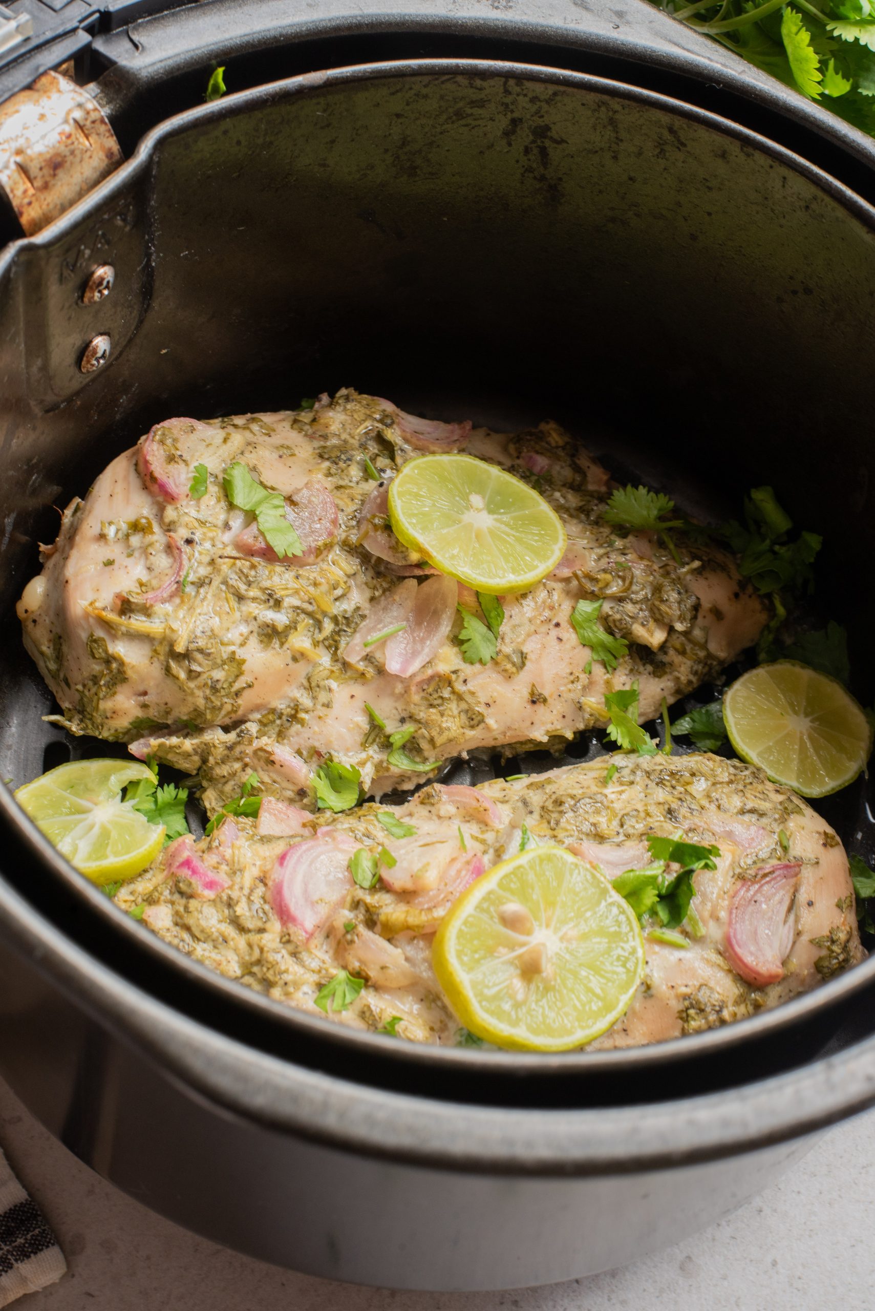 Two seasoned chicken breasts, inspired by Marinated Yogurt Herb Chicken, are topped with lime slices and herbs, then cooked to perfection in a black slow cooker.