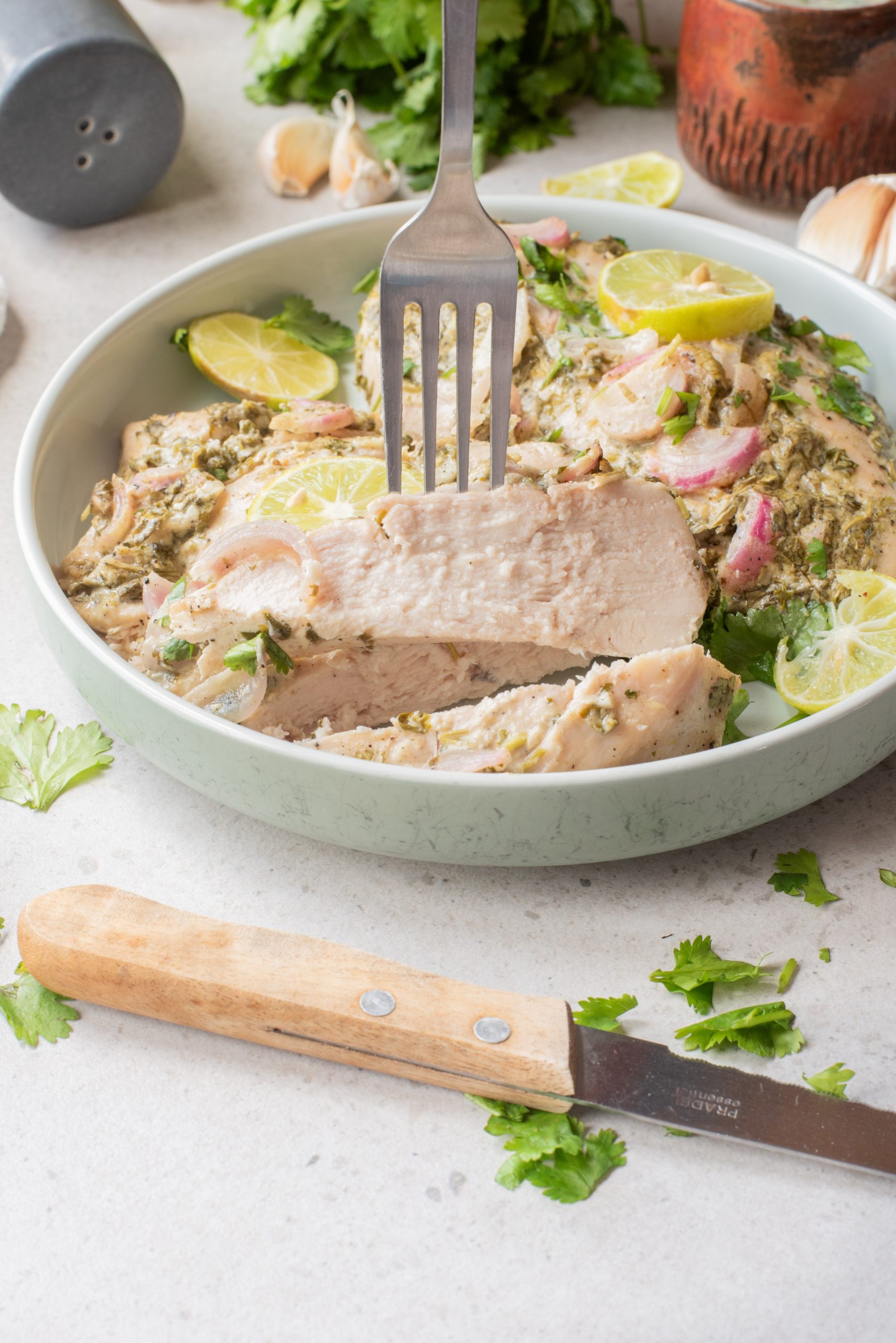 A fork holds a thick slice of cooked pork garnished with lime and herbs in a round dish, reminiscent of the fresh flavors found in Air Fryer Cilantro Lime Chicken, with a wooden-handled knife resting nearby.