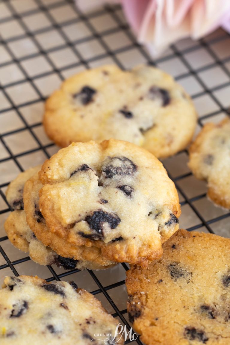 A close-up of several Dried Blueberry Lemon Cookies cooling on a black wire rack, their golden edges and fruity aroma inviting you to enjoy a fresh-baked treat.