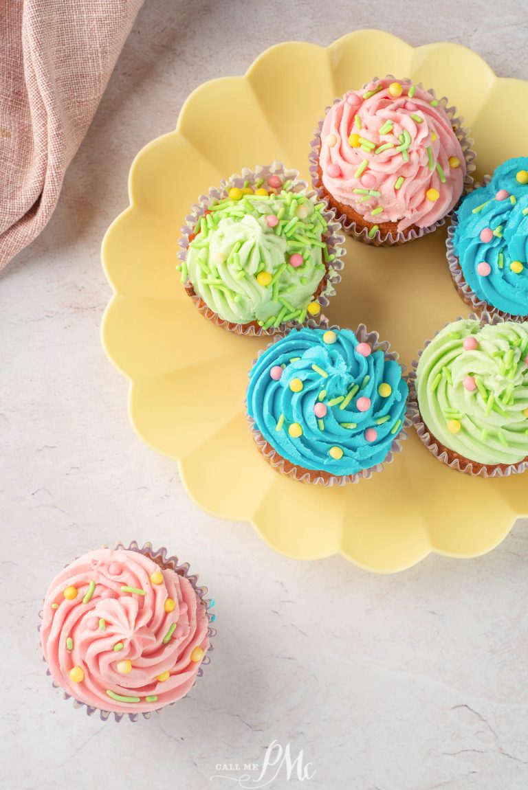 Six cupcakes with pink, green, and blue frosting and colorful sprinkles are arranged on a yellow plate, with one green and pink cupcake placed next to the plate.
