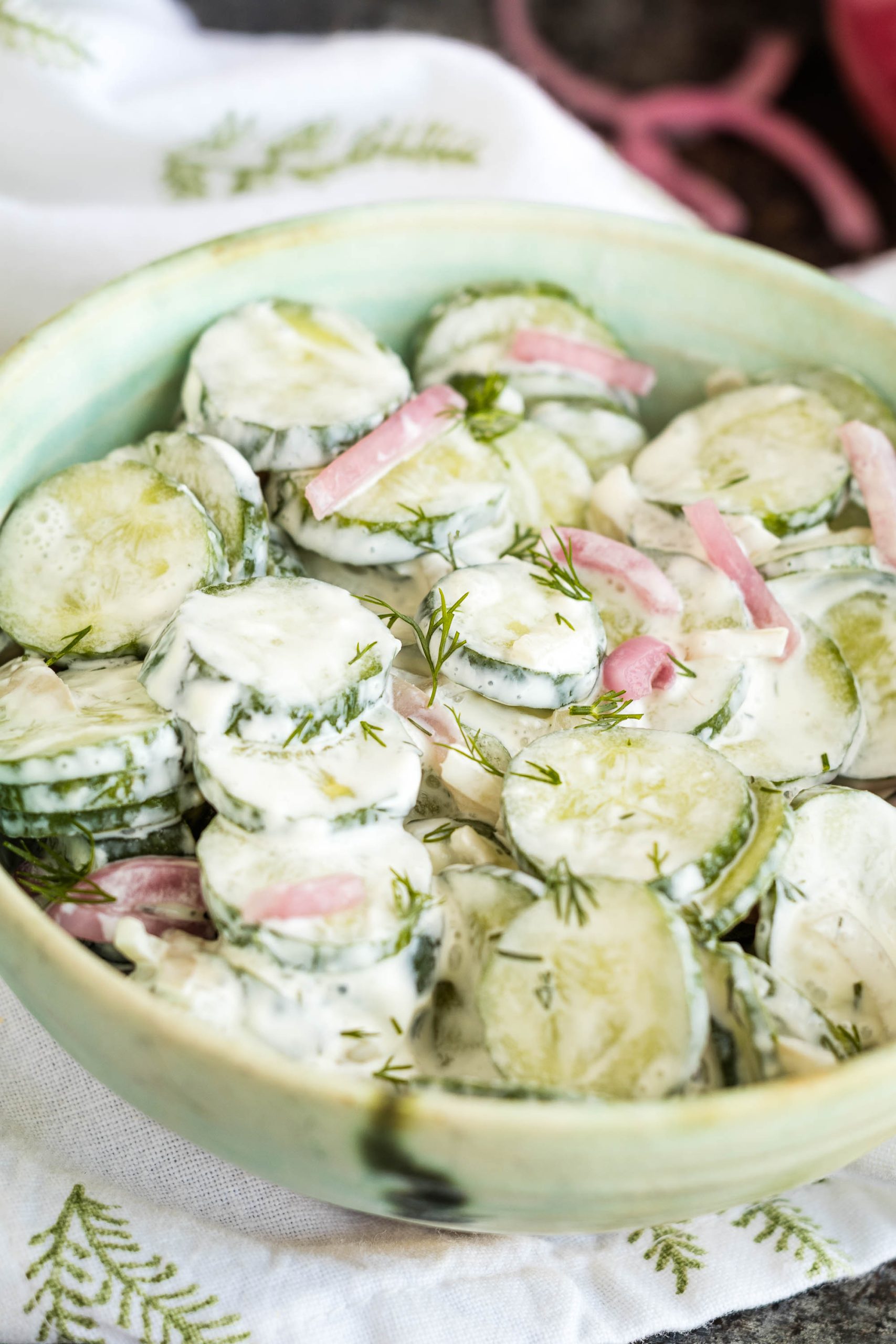 Bowl of cucumber salad with creamy dressing, fresh dill, and red onion slices.