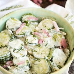 A bowl of creamy cucumber salad with sliced cucumbers, red onions, and fresh dill, served in a light green dish.