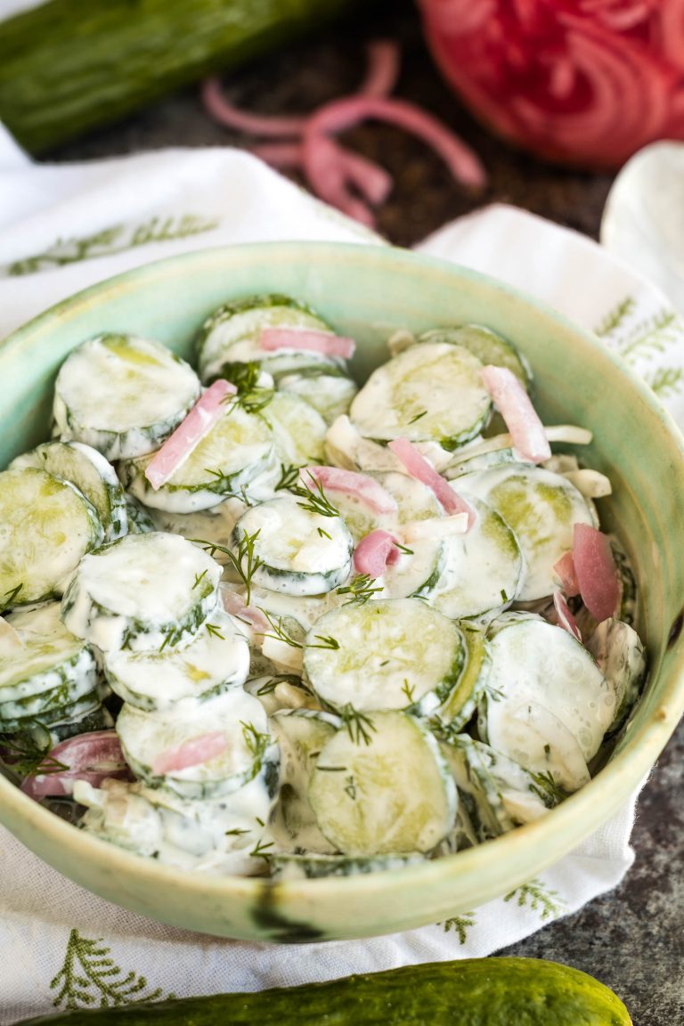 A bowl of creamy cucumber salad with sliced cucumbers, red onions, and fresh dill, served in a light green dish.