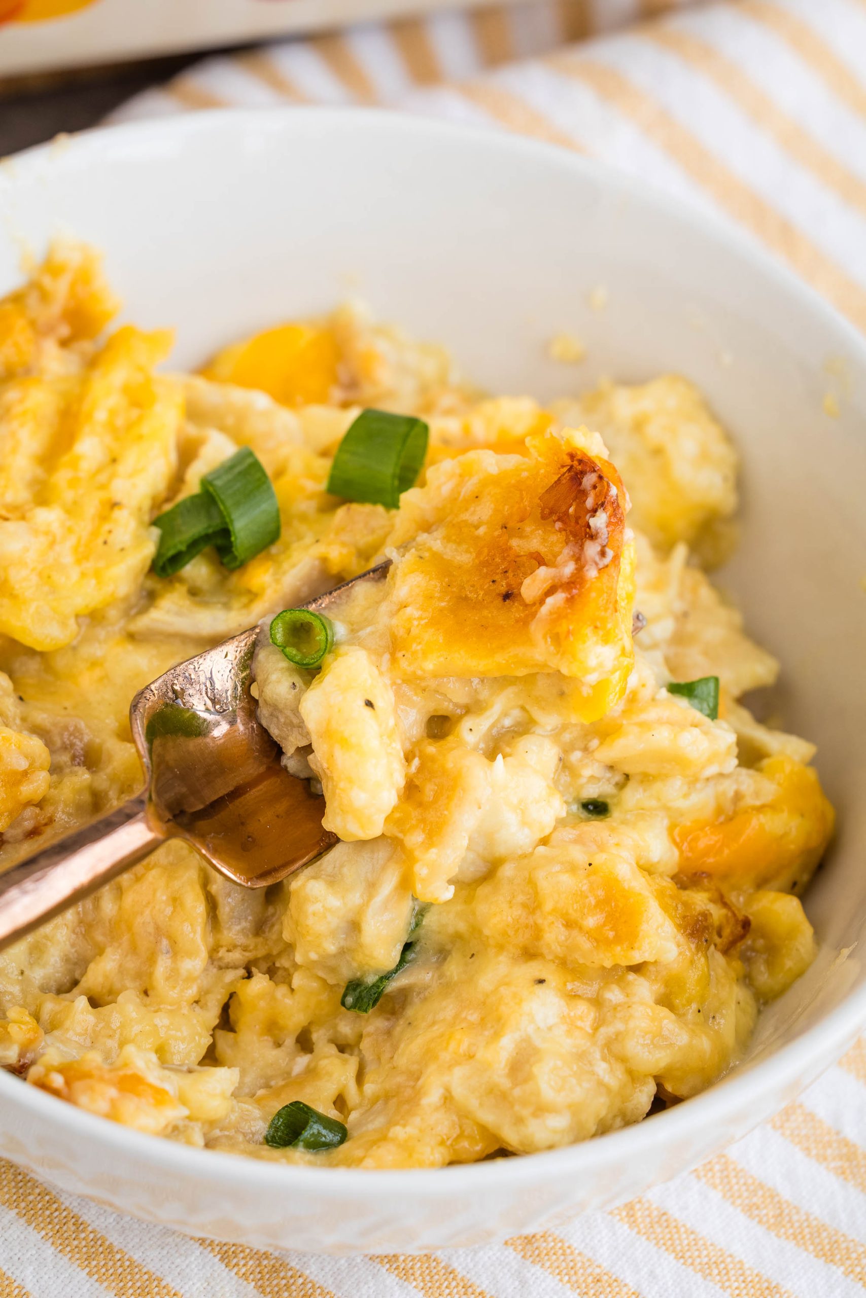 A close-up of a bowl of cheesy scrambled eggs, inspired by Dolly Parton's 5-ingredient Casserole, garnished with chopped green onions, with a fork lifting a portion.