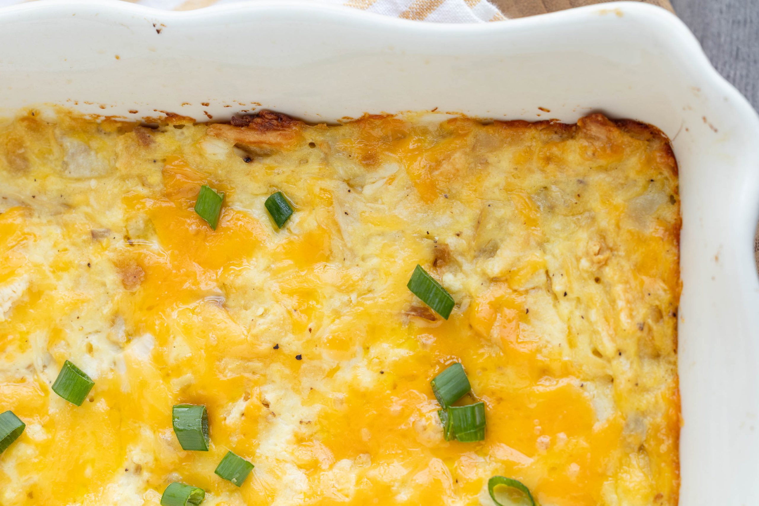 A baked recipe topped with melted cheese and garnished with chopped green onions in a white dish.