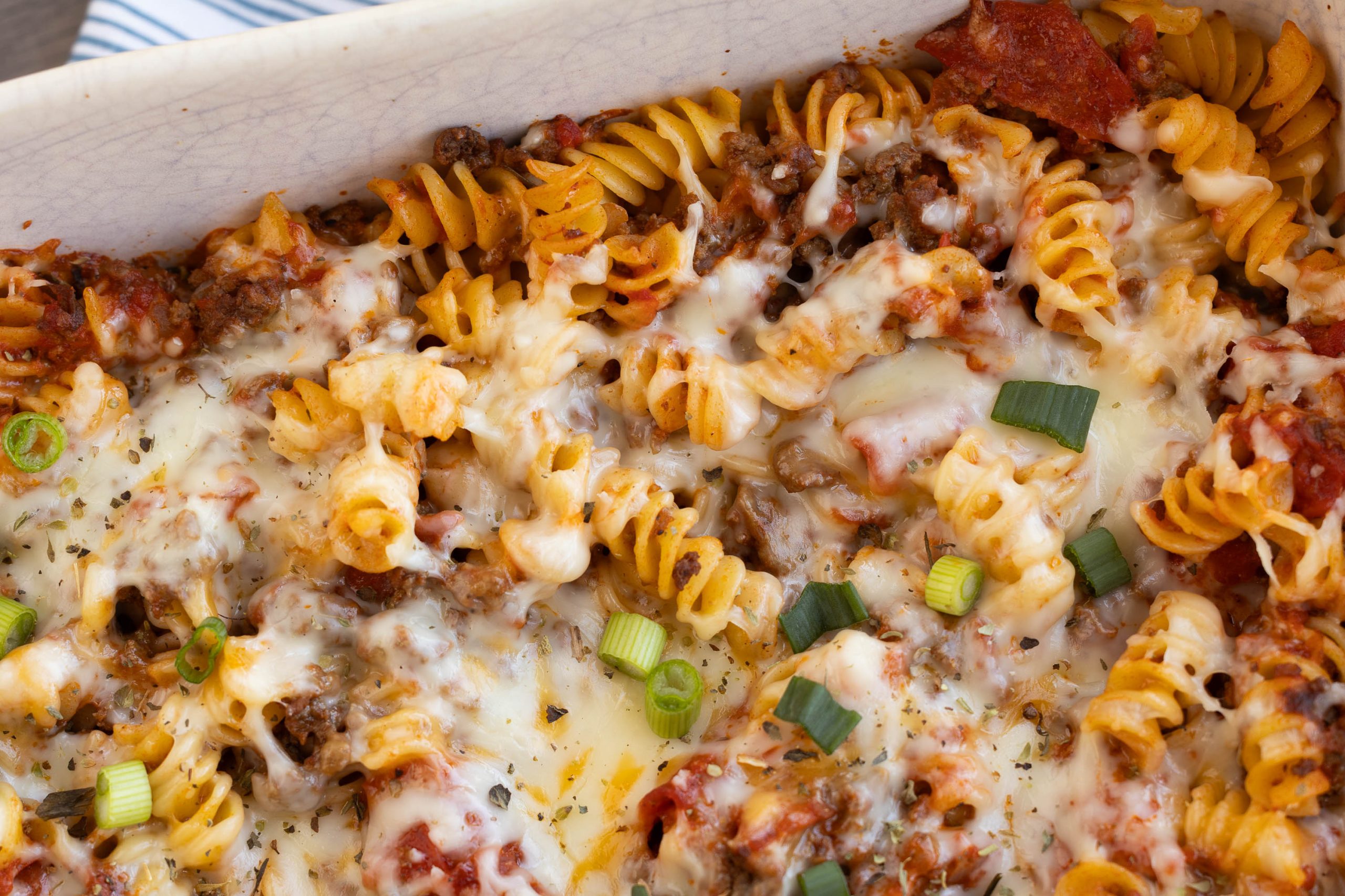 White baking dish with melted cheese, ground meat, tomato sauce, and sliced green onions in a white baking dish.