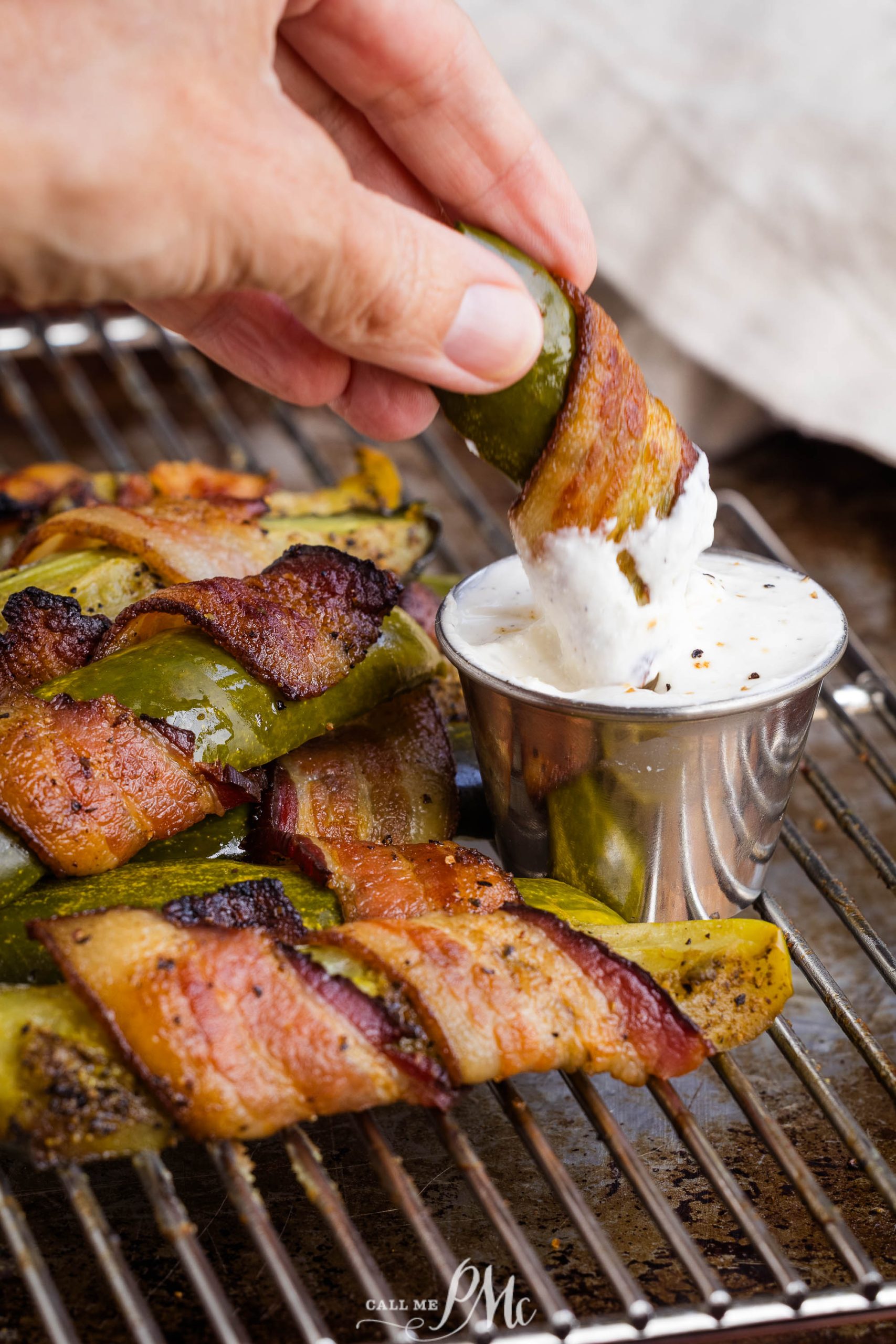 A hand dips an appetizer into a cup of creamy white sauce.