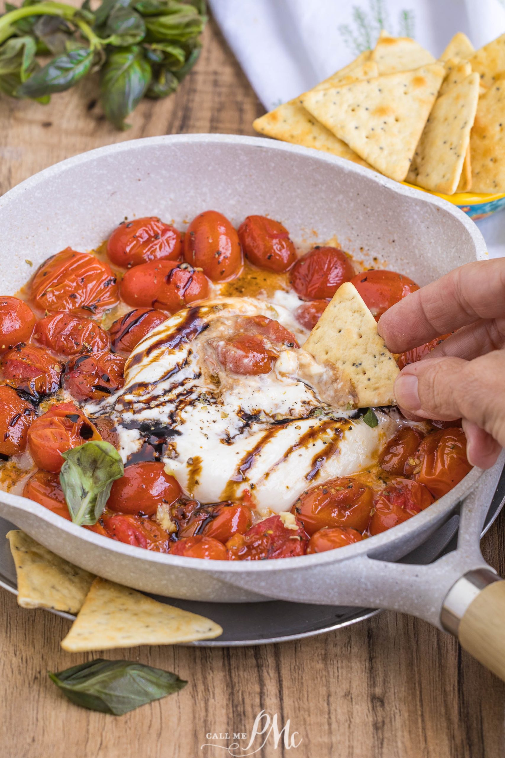 An appetizer with a hand dipping a cracker into the cheese.