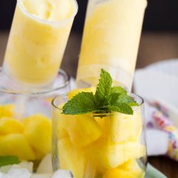 Glass filled with pineapple chunks and mint leaves, with two yellow frozen popsicles in the background.