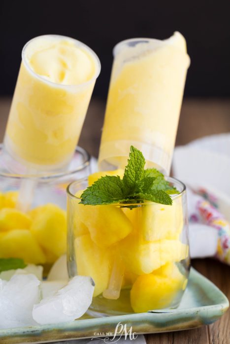 Glass filled with pineapple chunks and mint leaves, with two yellow frozen popsicles in the background.