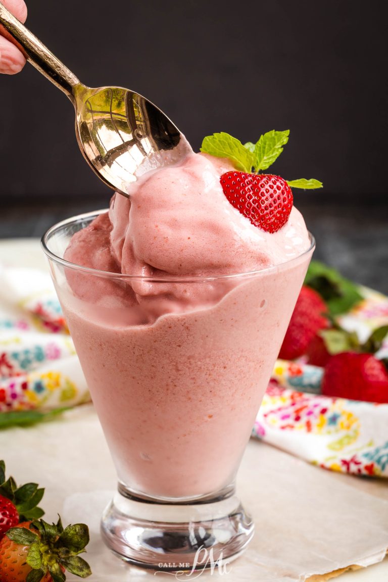 A spoon scoops pink Boozy Strawberry Dole Whip served in a glass, topped with a fresh strawberry and mint leaf.