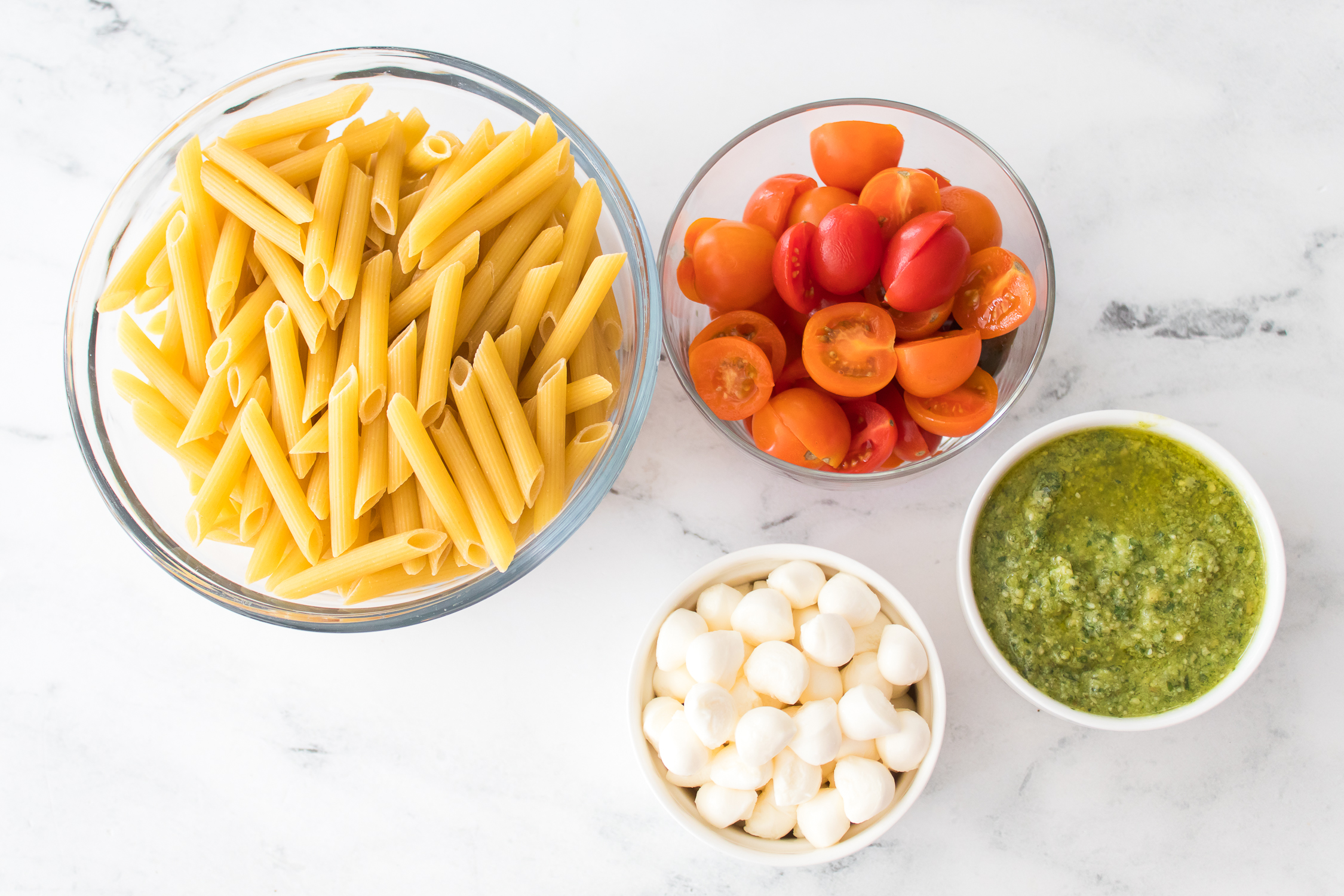 Four bowls with ingredients—await assembly on a white marble surface.