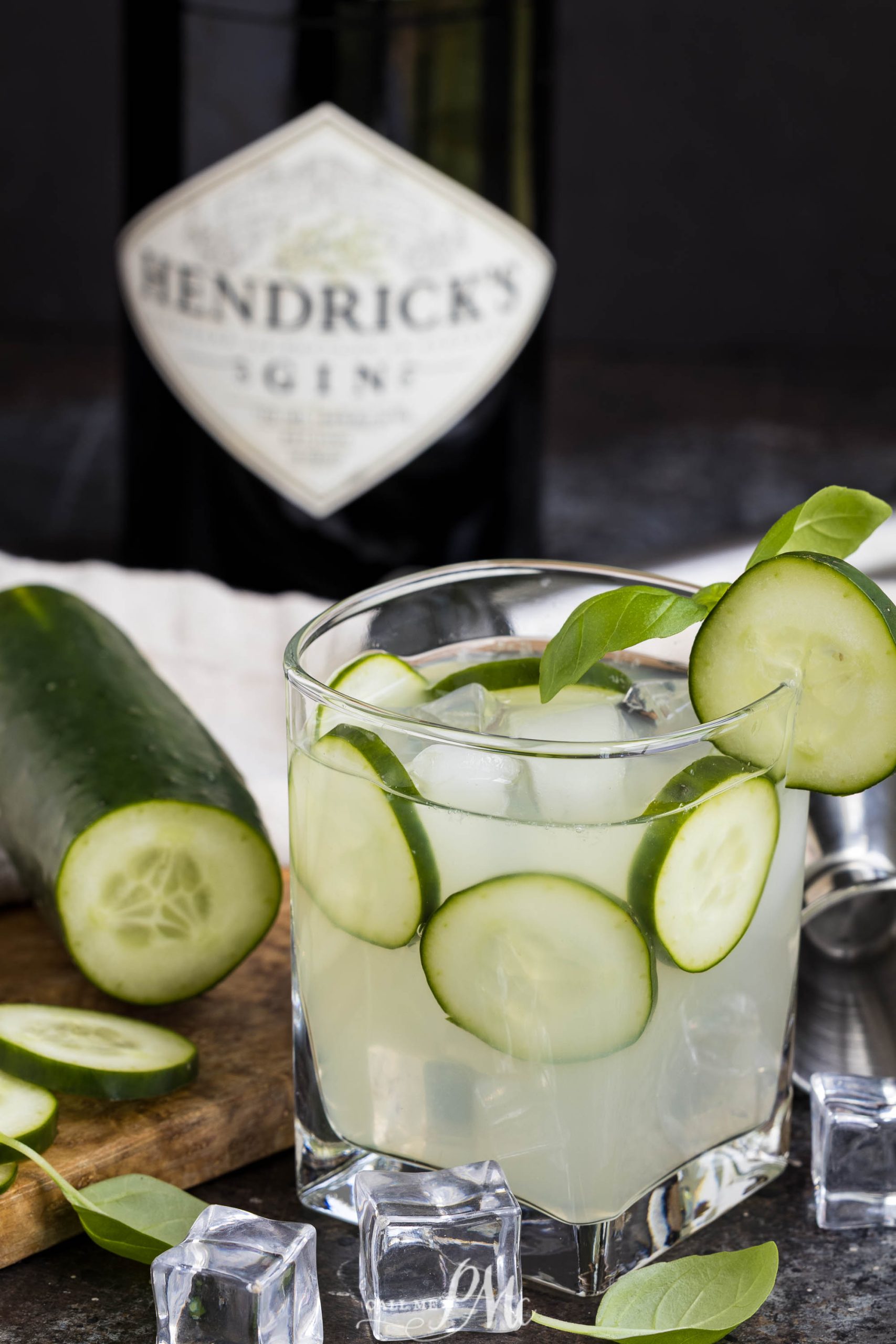 A drink sits in front of a  bottle and a cutting board.