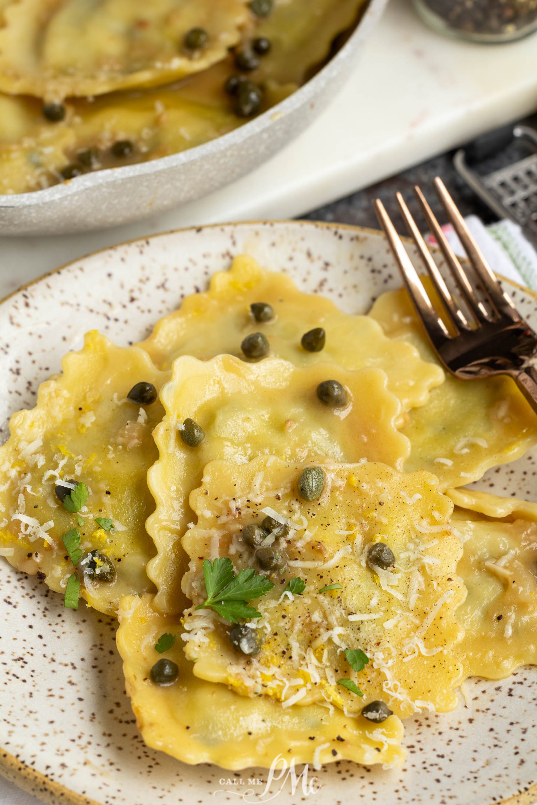 A plate of pasta topped with grated cheese, capers, herbs, and black pepper, with a fork beside the pasta.