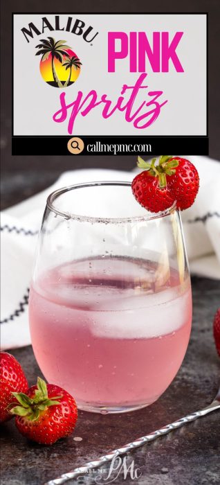 A glass of liquid garnished with fresh strawberries sits on a table, with a striped napkin and more strawberries nearby.