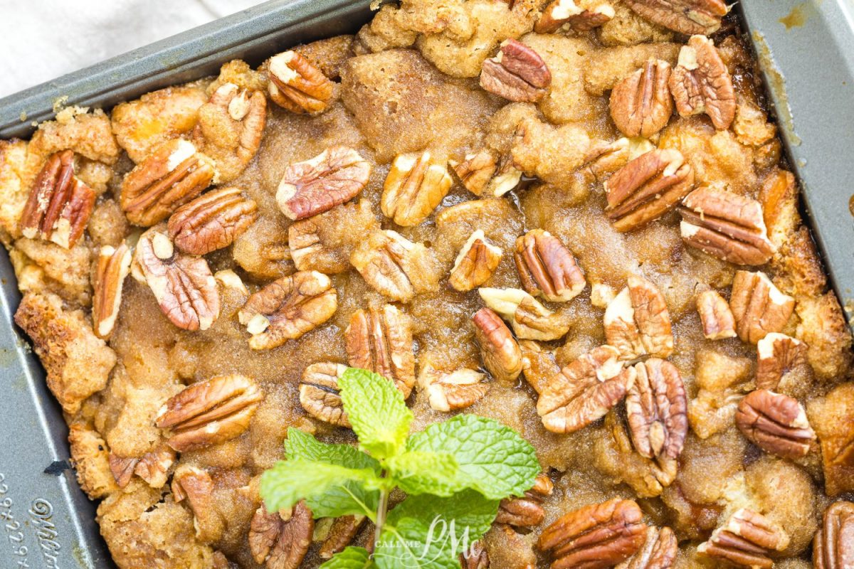 A close-up of a baked dessert in a rectangular pan topped with pecan halves, golden brown crumbly topping, and a fresh mint sprig in the center.