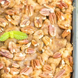 A baked dessert in a square pan topped with pecan halves and a sprig of fresh mint, featuring a golden-brown, crumbly surface.