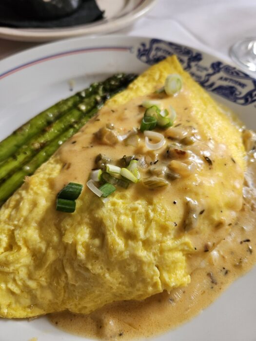 A fluffy omelette topped with creamy sauce and chopped green onions, served with asparagus spears on a decorative plate.
