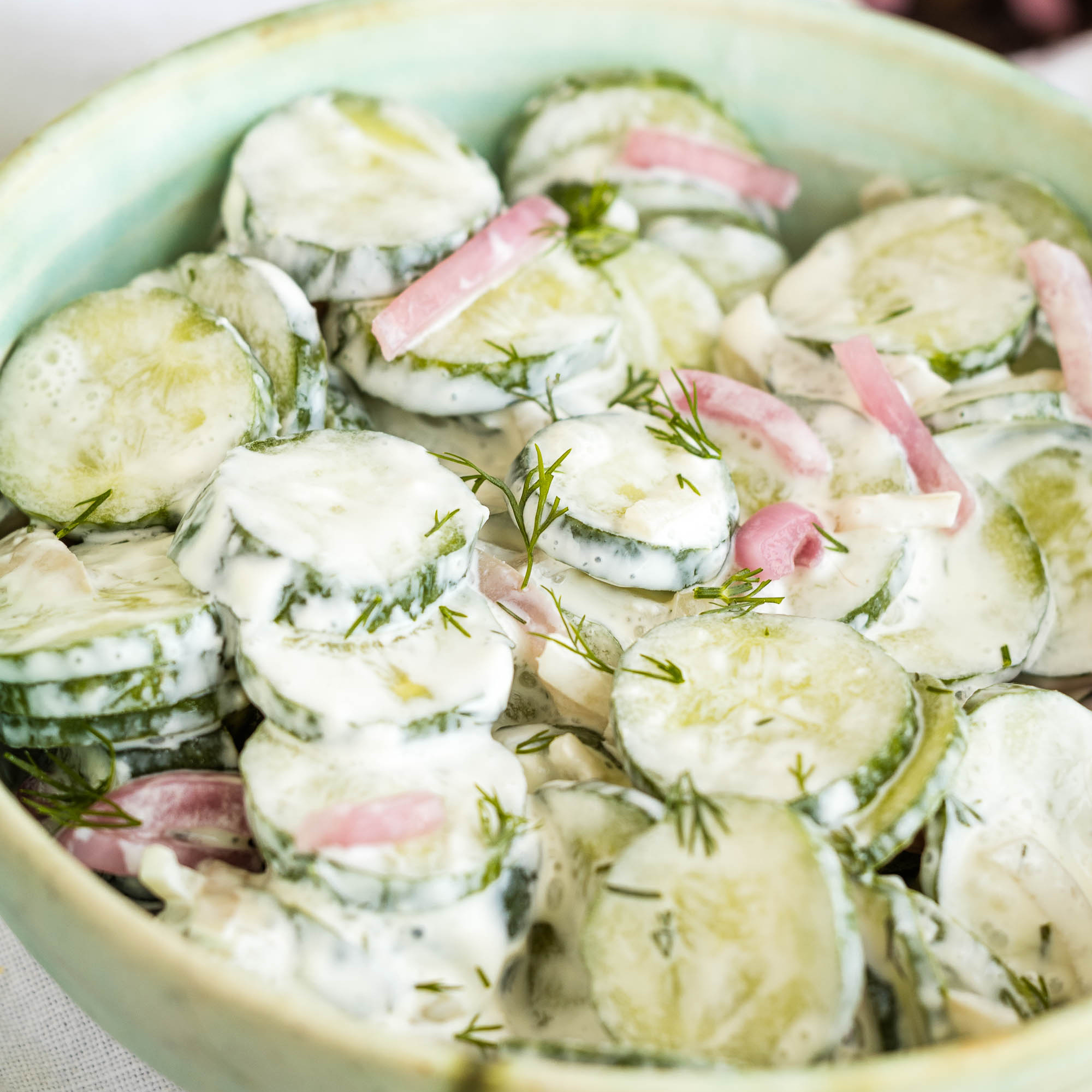 A bowl of creamy cucumber salad with sliced cucumbers, thinly sliced red onions, and fresh dill, all coated in a white, creamy dressing.