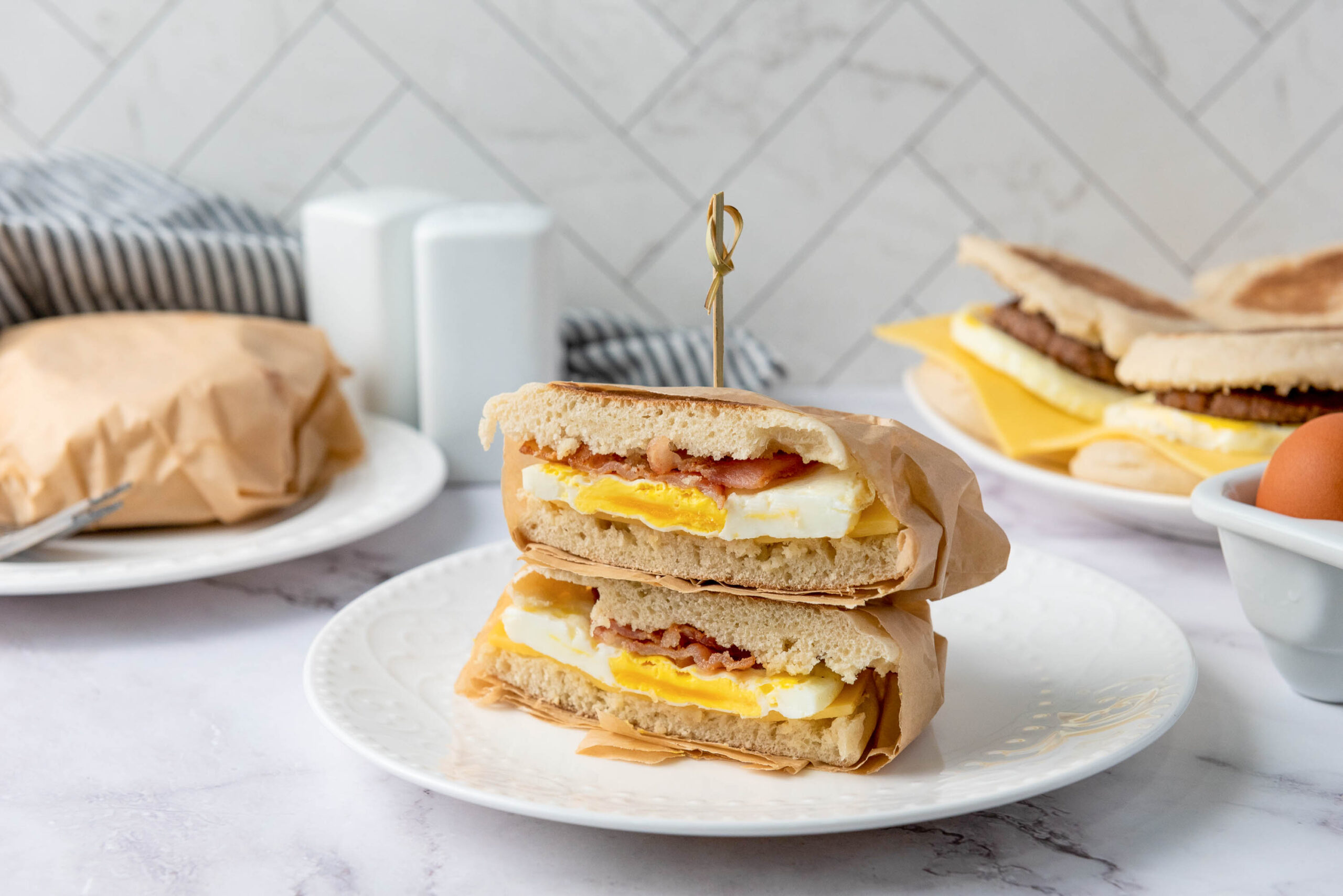 A meal prep breakfast is cut in half and stacked on a white plate. In the background, more sit with a brown egg are visible on a marble counter.