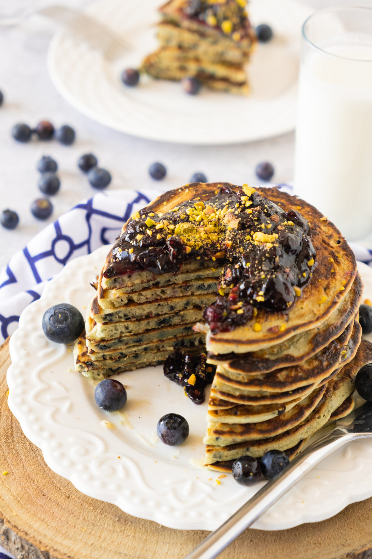Fluffy gluten-free breakfast served on a white plate. A fork and a glass of milk are nearby, with more pancakes in the background.