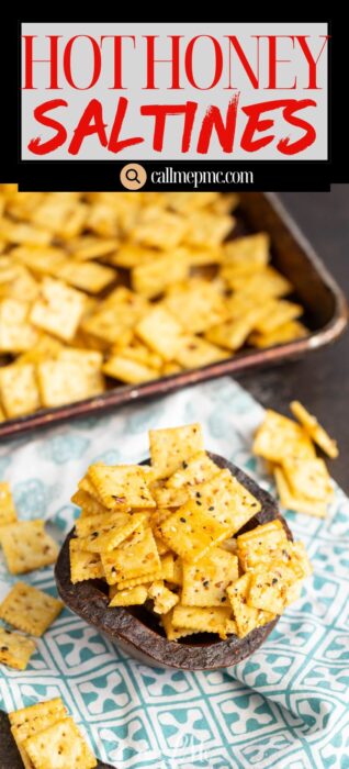 A small bowl filled with seasoned saltine crackers sits on a patterned cloth, with more crackers scattered nearby and a baking tray of crackers in the background. Text at the top reads, “Hot Honey Saltines.”.