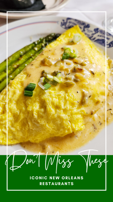 A close-up of a creamy omelet topped with green onions, served with asparagus spears on a white plate. Text overlay reads: “Don’t Miss These: Iconic New Orleans Restaurants.”.