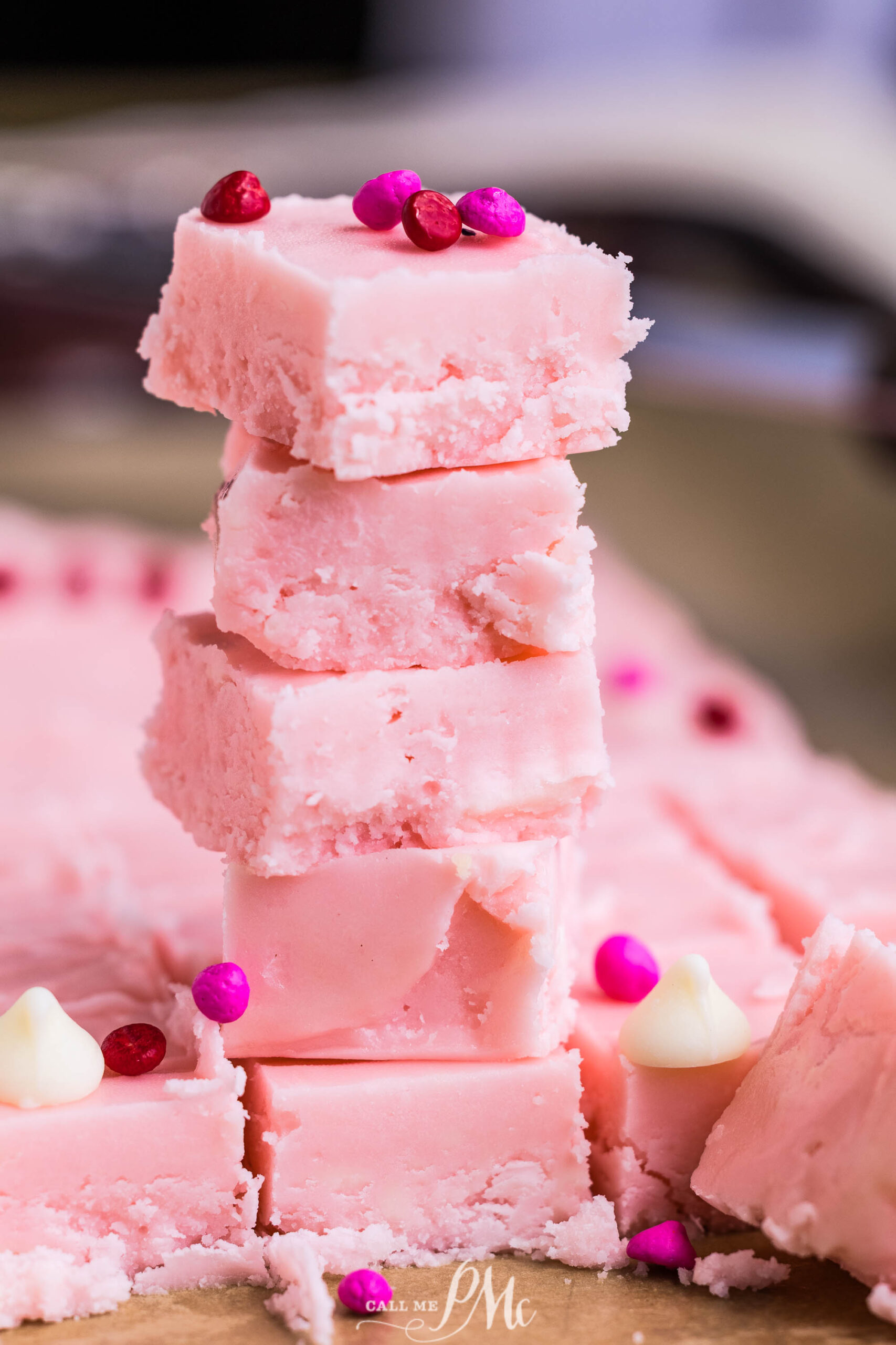 A stack dessert squares with a smooth texture, topped with pink and red candy sprinkles scattered in the background.